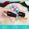 A hand holds a digital device displaying 0.00, surrounded by colorful play balls on a white fluffy surface.