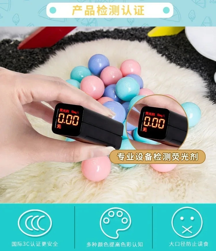A hand holds a digital device displaying 0.00, surrounded by colorful play balls on a white fluffy surface.