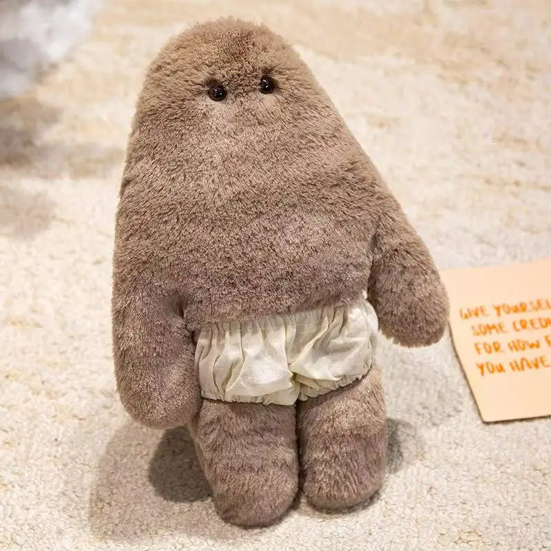 A soft, brown monster plush doll with a ruffled skirt is shown on a light background.
