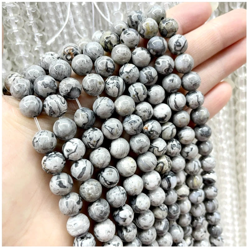 A hand holds a strand of natural stone beads for DIY jewelry making featuring various colors and patterns.