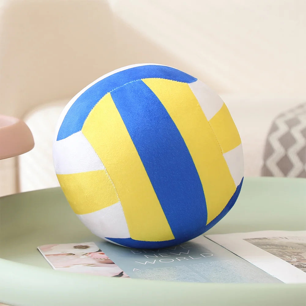 A blue and yellow soft plush volleyball pillow resting on a light green surface.