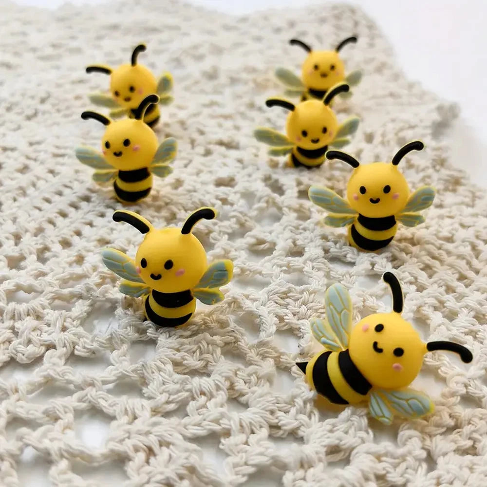 A collection of yellow and black 3D bee silicone beads for DIY crafts displayed on a cream-colored crocheted surface.