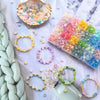 A collection of colorful frosted golden foil acrylic beads and jewelry findings arranged on white fabric.