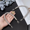 A hand holds a sparkling rhinestone purse strap bracelet with a coin charm against a black background.