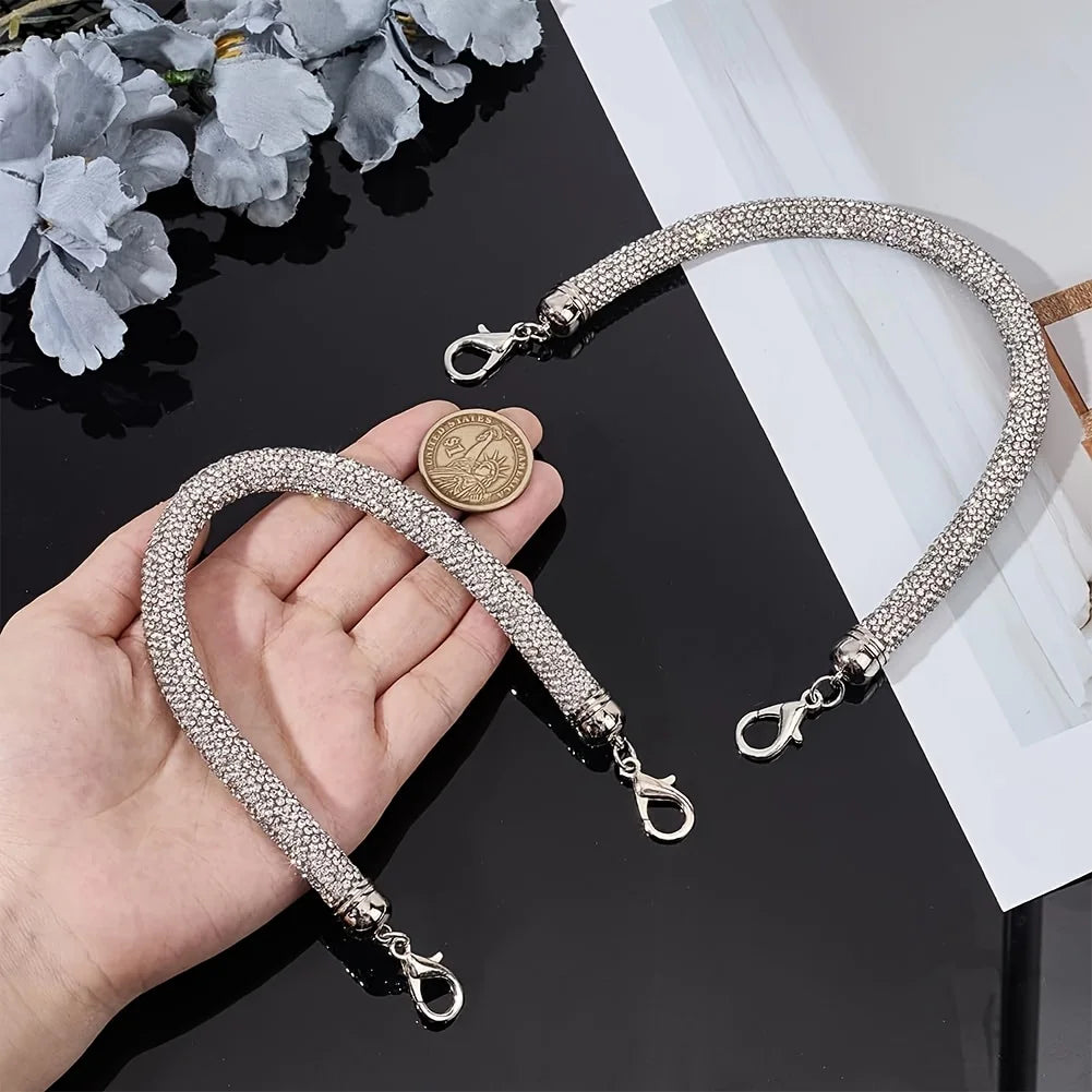 A hand holds a sparkling rhinestone purse strap bracelet with a coin charm against a black background.