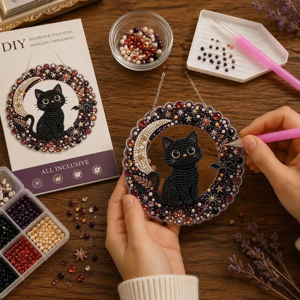 A hand holds a finished diamond painting hanging ornament featuring a black cat surrounded by sparkling jewels.