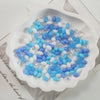 A white dish filled with oval glass rice grain beads in shades of blue and white for jewelry making