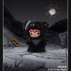 A dark, fluffy black plush doll with pink accents sits in a snowy outdoor setting under a night sky.