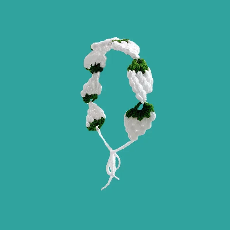 A white strawberry crochet headband with a wide elastic band against a teal background.