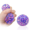 A hand holds a purple and pink water bead stress ball, showing its translucent texture and colorful beads.