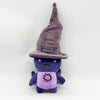 A purple plush rabbit toy wearing a witch hat and a purple shirt with a sun design.