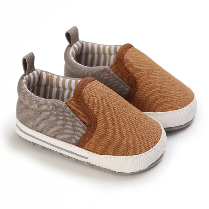 A pair of tan and gray baby first walker sneakers with striped lining and dinosaur print details.
