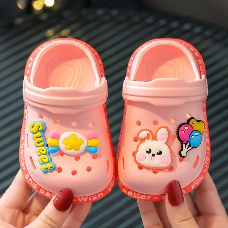 A pair of pink lightweight children's clogs with a white rabbit design are held in a hand.
