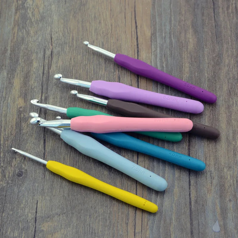 A collection of colorful ergonomic crochet hooks, stitch markers, and needles arranged on a wooden surface.