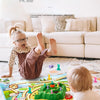 A toddler plays with a colorful rabbit trap puzzle game on the floor in a bright living room setting.