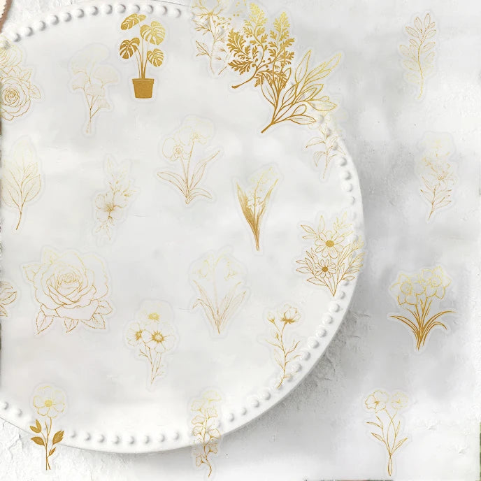 A round clear sticker pack featuring delicate gold botanical illustrations on a white background.