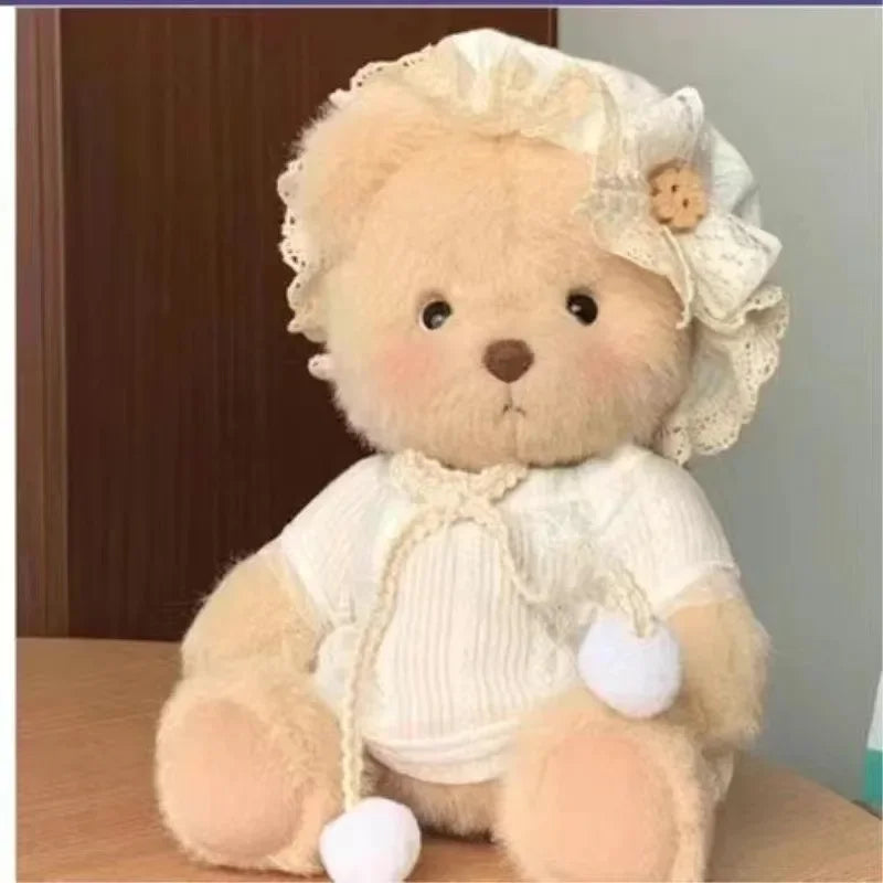 A light beige teddy bear plush wearing a white lace dress and featuring small white pom-poms.