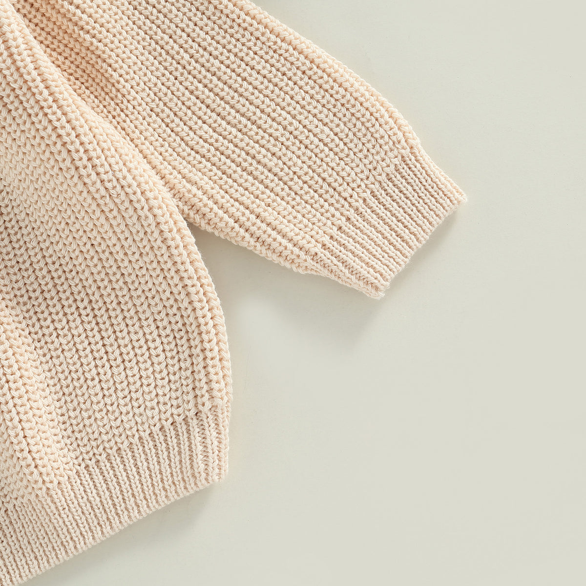 A close-up of a light beige knit long sleeve sweater for kids.