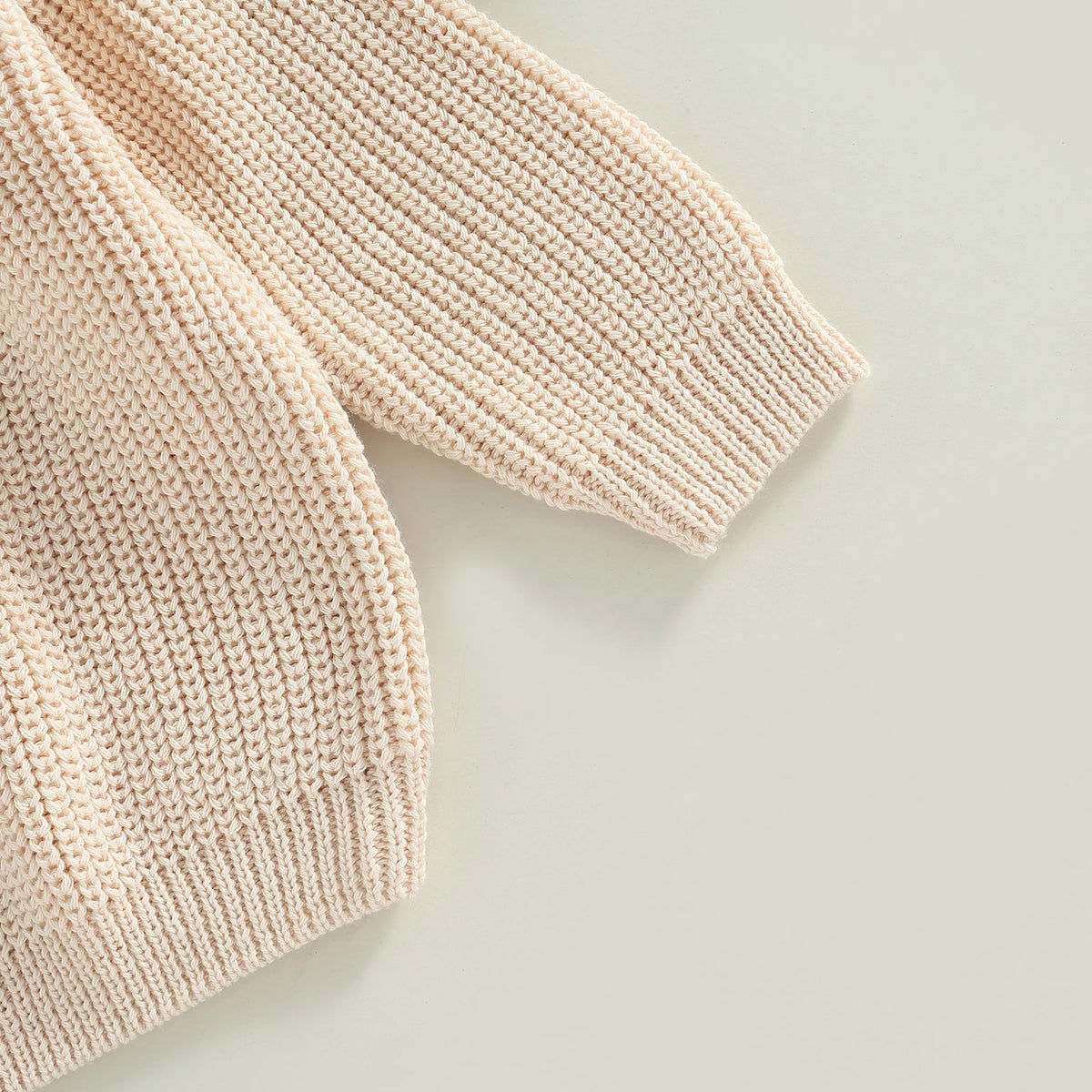 A close-up of a light beige knit pullover sweater with a textured stitch pattern.