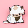 A white cat enamel pin featuring a cute face with brown accents, shown against a pink background.