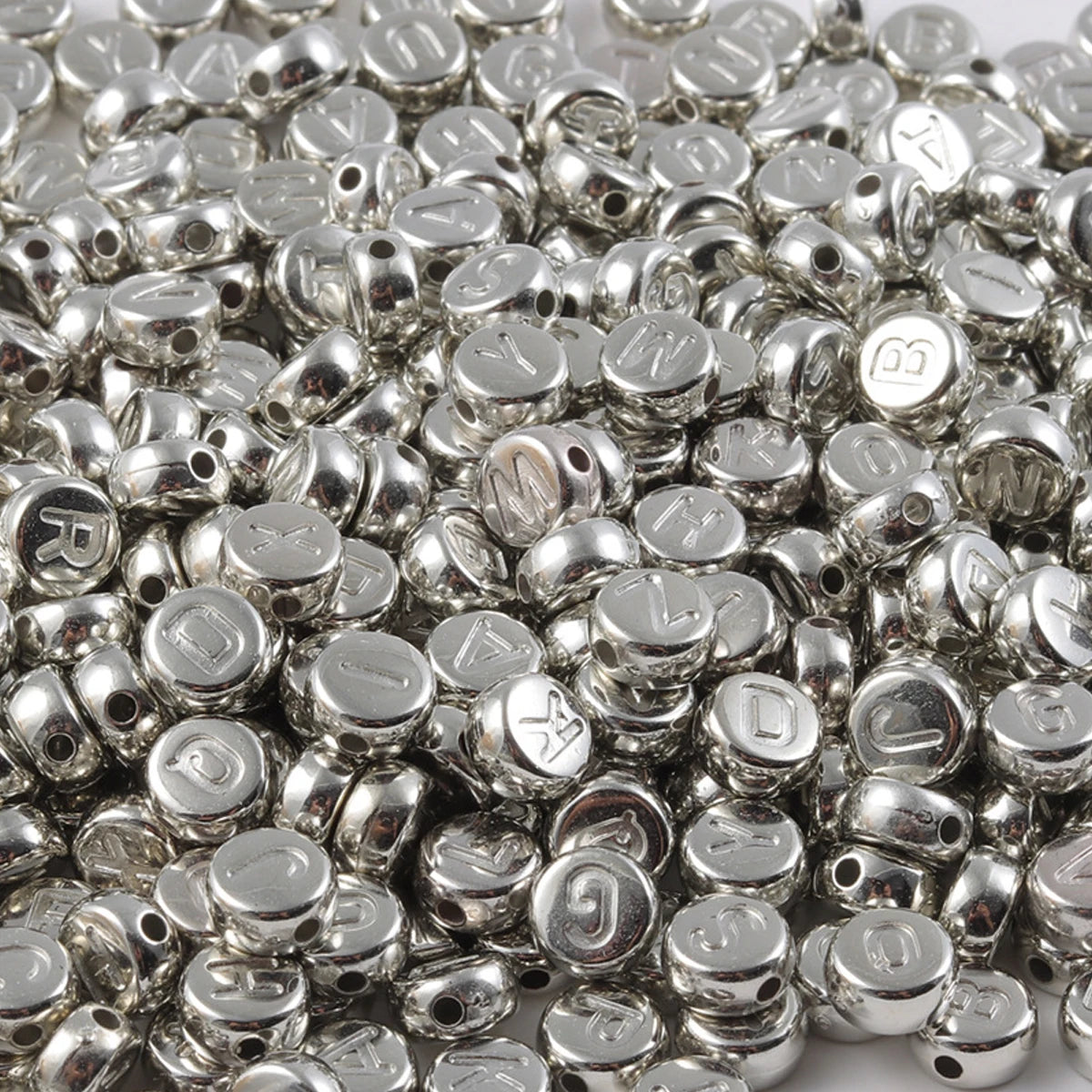 A pile of small silver acrylic alphabet beads for jewelry making