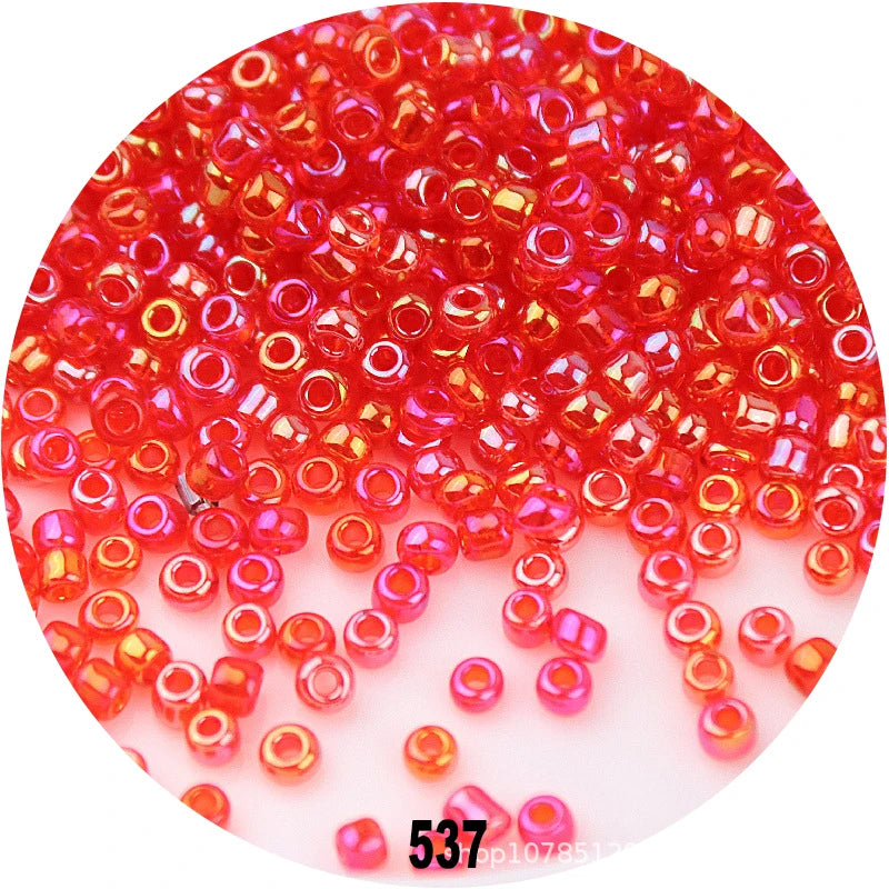 A close-up view of numerous colorful round loose glass seed beads in various shades of red and pink.