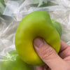 A hand holds a bright lime green, oval-shaped stress ball with a squishy texture inside a clear plastic bag.