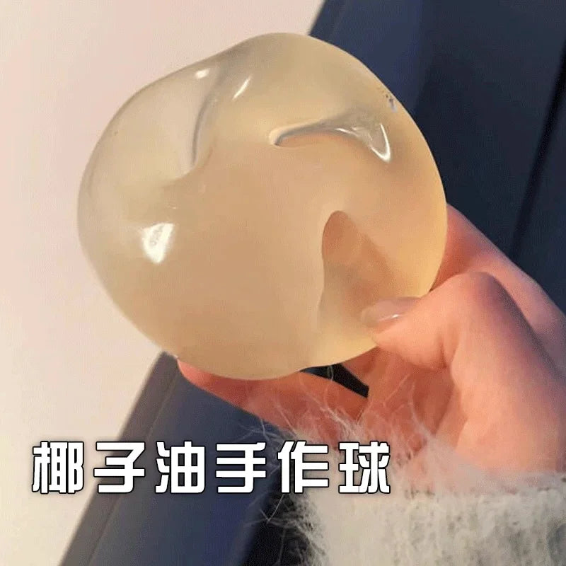 A translucent, pale yellow squishy stress relief fidget toy is held in a person's hand against a dark background.