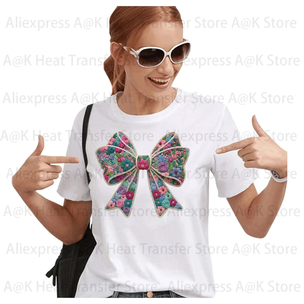 A woman models a white t-shirt featuring a large floral letter bow iron-on patch on the chest.