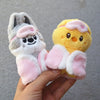 A hand holds a yellow cartoon animal plush toy with pink accents and a gray cartoon animal plush toy.
