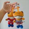 An orange plush toy of El Sapo Concho with a black mustache and a red shirt, held by a hand.