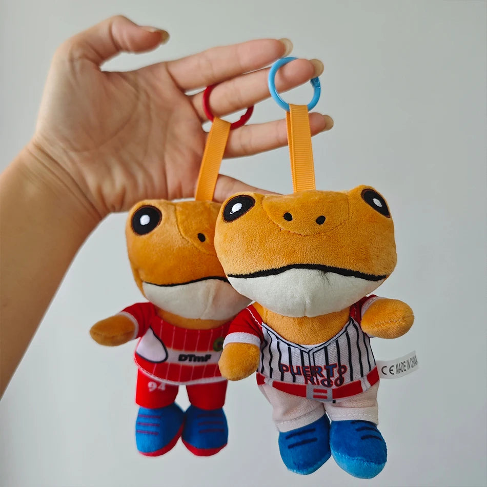 An orange plush toy of El Sapo Concho with a black mustache and a red shirt, held by a hand.