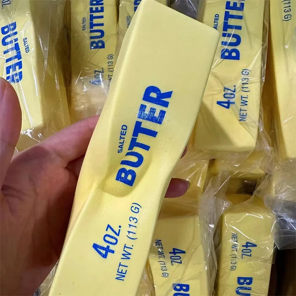 A hand holds a yellow butter squishy stress relief toy packaged in plastic.