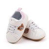 A pair of light beige baby sneakers with pink accents and a cute brown bear design.