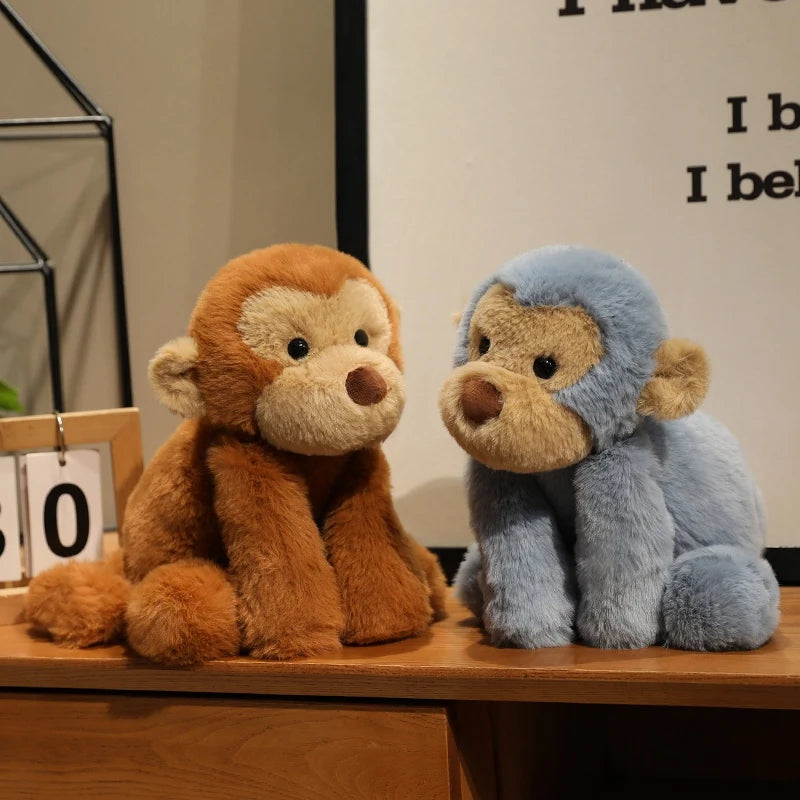 A pair of soft plush monkey toys, one brown and one blue, sitting on a wooden surface.