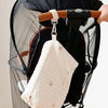 A quilted white baby diaper caddy organizer hanging from a brown leather strap on a black stroller.