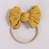 A mustard yellow fabric bow headband with a light beige elastic band.