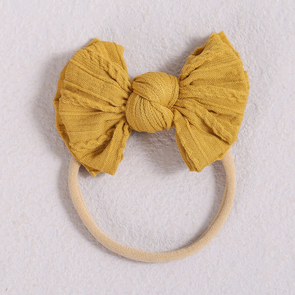 A mustard yellow fabric bow headband with a light beige elastic band.