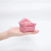 A hand holds a miniature red and white striped sofa and pillow set for a dollhouse.