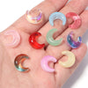 A collection of moon-shaped glass beads in various colors including pink, blue, green, and red, displayed on a hand.