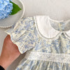 A close-up of a light blue floral dress for girls featuring puff sleeves and a white Peter Pan collar with lace trim.
