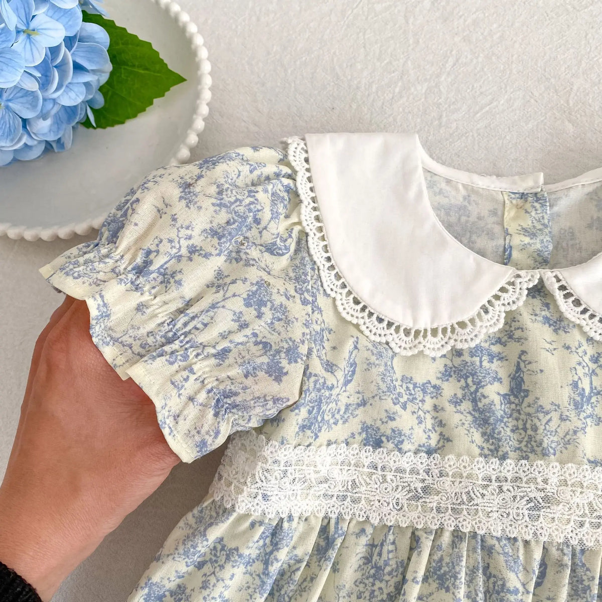 A close-up of a light blue floral dress for girls featuring puff sleeves and a white Peter Pan collar with lace trim.