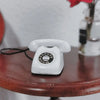 A white vintage rotary telephone miniature resting on a dark wooden surface.