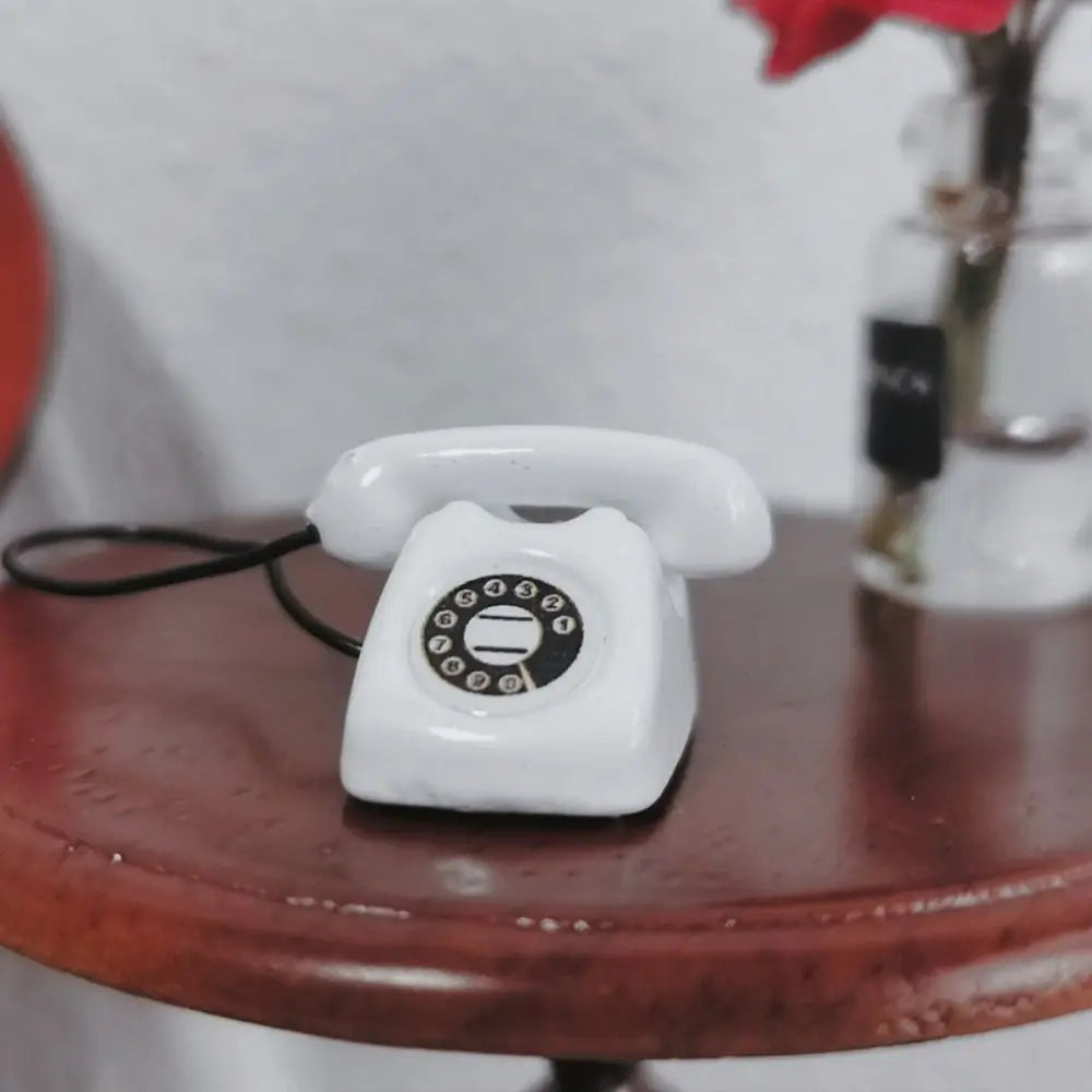 A white vintage rotary telephone miniature resting on a dark wooden surface.