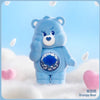 A blue Grumpy Bear Care Bear plush toy standing in soft white snow with falling snowflakes.