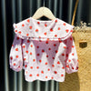 Pink long-sleeve shirt for a baby girl with a strawberry print displayed on a wooden hanger.