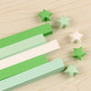 A collection of green and white origami star strips scattered on a light wooden surface.