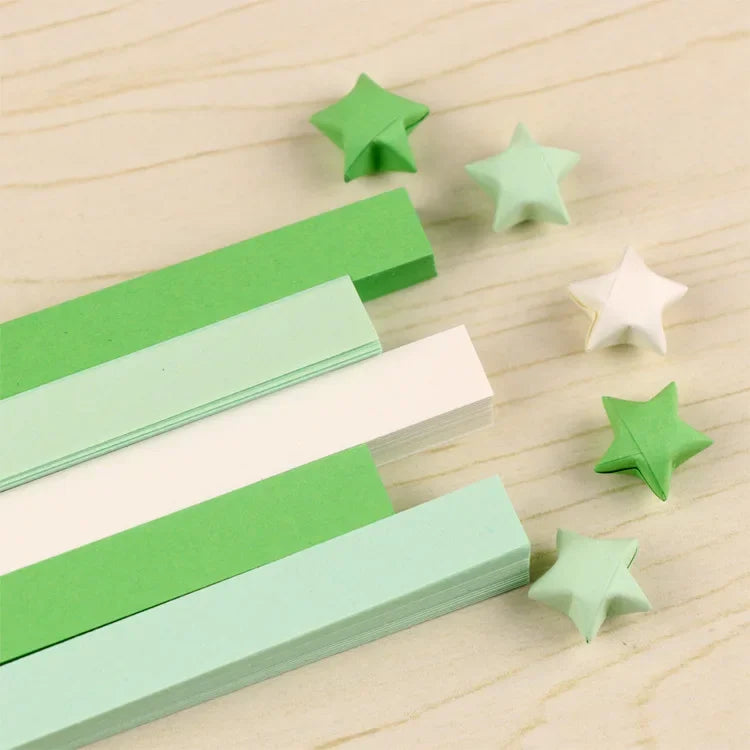A collection of green and white origami star strips scattered on a light wooden surface.