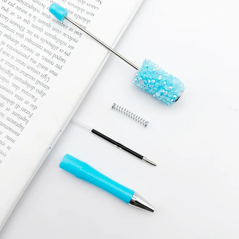 A collection of diamond sequin bead ballpoint pens and a metal spring are displayed on a white background.