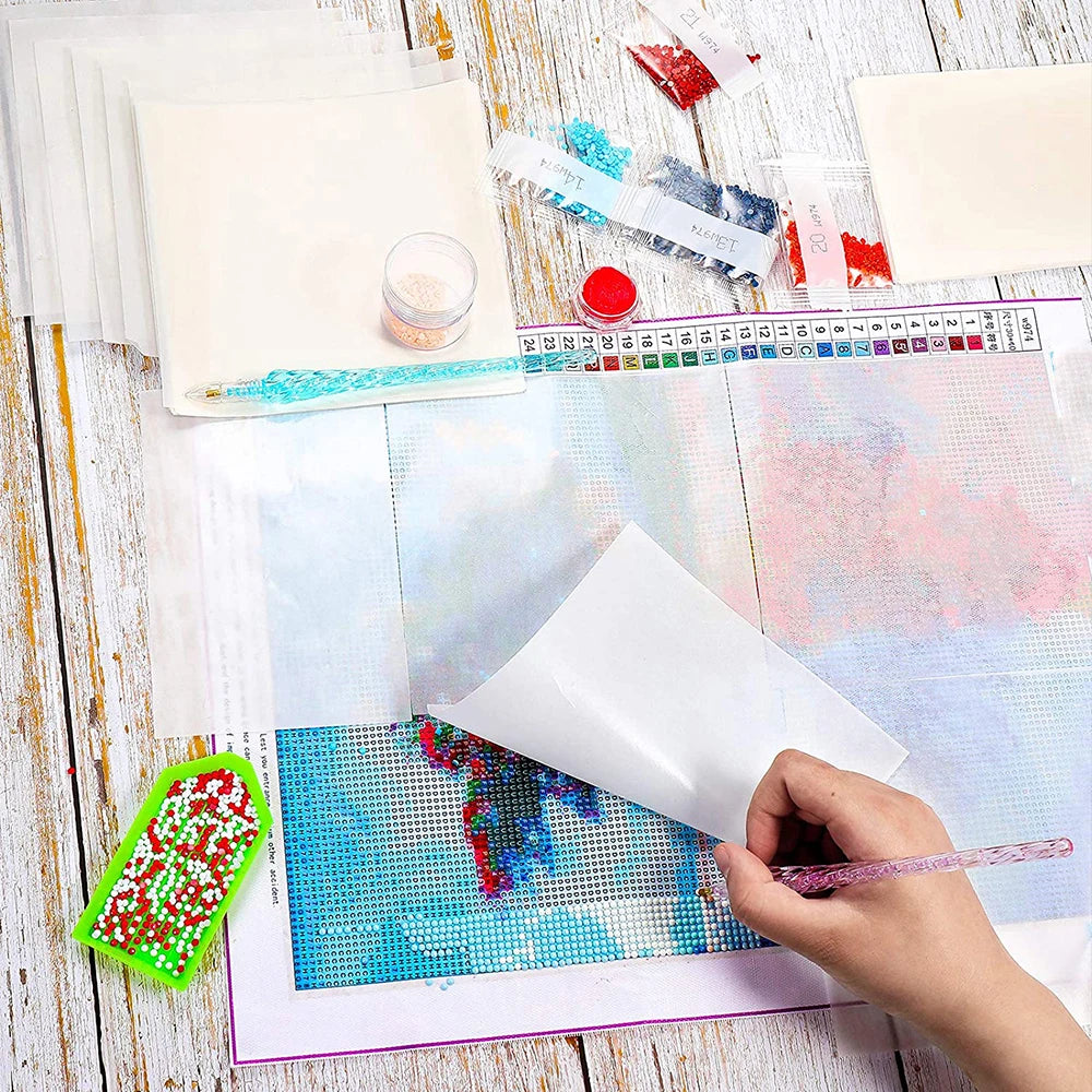 A hand is placing glitter onto a sheet of double-sided non-stick release paper for diamond painting.